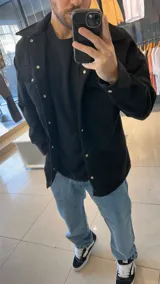 Chaqueta negra de paño con cuello clásico, cierre frontal con botones a presión, dos bolsillos de parche en el pecho y corte holgado.