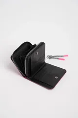 Billetera cuadrada color fucsia con cierre de cremallera y tirador con diseño de zigzag. Tiene un parche circular con borde dorado y un corazón rosa en el centro.