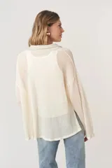 Sweater de malla color crudo, con cuello polo gris acanalado, mangas largas holgadas y ruedo desflecado.