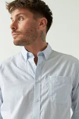 Camisa celeste a rayas rojas de hombre, manga larga, con bolsillo y logo bordado.