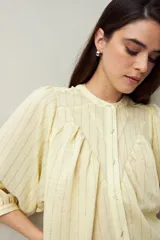 Camisa celeste a rayas verticales, de corte amplio y mangas 3/4. Presenta cuello mao, cierre frontal con botones irregulares y detalle de pespuntes y pinzas en el canesú.