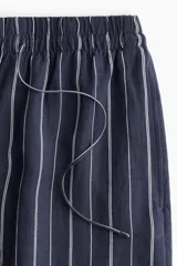 Pantalón de corte holgado en tejido liviano de mezcla de lino a rayas verticales blancas y azul marino. Modelo de tiro alto con cintura elástica y cordón para ajustar fino, bolsillos laterales discretos y piernas rectas.