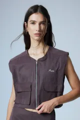 Chaleco corto color marrón confeccionado en gabardina con cierre metálico frontal, bolsillos con fuelle y badana de PU en la espalda.