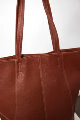Bolso tote de cuero marrón con costuras a la vista y doble bolsillo interior, uno con cierre. Cierra con broche imán.