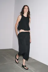 Falda midi negra de tiro alto con cintura elástica y frunces. Presenta detalle de tejido combinado y abertura en la parte trasera del ruedo.