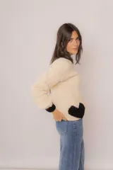 Sweater tejido de lana merino color crema, con cuello redondo y puños negros. Tiene un corazón negro en el frente.