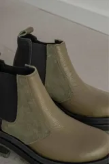 Botines Chelsea de cuero color verde oliva y negro, con elásticos laterales negros, tirador trasero y suela track de goma color verde oliva.