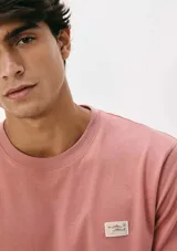 Camiseta blanca de algodón con cuello redondo y mangas cortas. Estampa rectangular con borde negro que contiene la frase "NATURAL ATMOSPHERE" en letras mayúsculas y una imagen de montañas y mar.