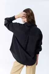 Camisa negra de manga larga con cuello clásico, cierre frontal con botones y dos bolsillos con solapa en el pecho.