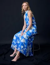 Vestido largo de gasa con estampado floral en tonos celeste y blanco. Tiene escote halter, cintura elastizada con lazo de ajuste, abertura en la espalda con botones y forro interno.
