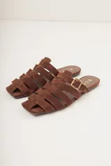 Sandalias planas de cuero color marrón con diseño de tiras entrecruzadas y hebilla lateral ajustable.