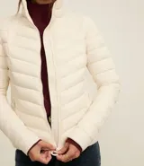 Campera puffer ultraligera color marrón, confeccionada en poliamida acolchada, con cuello alto y cierre por cremallera. Incluye bolsita con cordón.