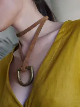 Collar con tira de cuero color suela y dije metálico dorado en forma de estribo.