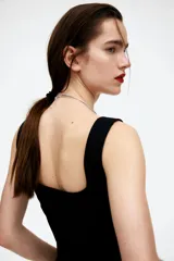 Musculosa negra con breteles anchos, escote cuadrado, cierre lateral oculto, pinzas en el busto y cintura entallada con costuras visibles.