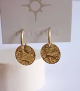 Par de aros colgantes dorados con forma de aro y dije circular con textura irregular.
