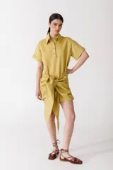 Vestido corto color pistacho, estilo camisa, con cuello clásico, mangas cortas con dobladillo y cierre frontal parcial con botones. Presenta un lazo anudado en la cintura.