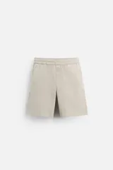 Bermuda color beige de corte relaxed fit, confeccionada en tejido de algodón. Cuenta con cintura elástica ajustable con cordón interior, bolsillos frontales y bolsillo trasero de parche.