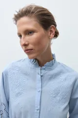 Camisa de algodón celeste claro, de manga larga, con cuello mao con volados y bordados calados florales en el frente y las mangas.