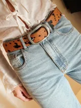 Cinturón de cuero con estampado animal print de vaca, hebilla metálica dorada y reverso de cuero color bordó.