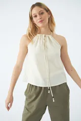 Blusa sin mangas color crudo, con cuello halter y cordón ajustable.