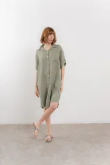 Vestido camisero corto color verde oliva, confeccionado en lino 100%. Tiene botones en la parte delantera, cuello camisero, mangas cortas con botón para arremangar y bolsillos laterales.