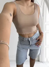 Musculosa ajustada de tejido acanalado (morley), con escote redondo y bordes ondulados en el ruedo. Disponible en colores beige, blanco y negro.