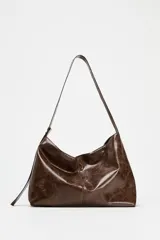 Bolso shopper marrón de efecto acharolado con asa de hombro ajustable, bolsillo interior con cremallera y cierre magnético.