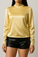 Blusa de satén color dorado, con cuello redondo, mangas largas abullonadas y puños camiseros.