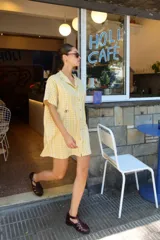 Vestido corto camisero a cuadros celestes y blancos, de corte amplio y cuello mao. Tiene botones a tono y logo bordado en el frente.