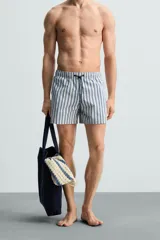 Bañador de hombre confeccionado en tejido técnico con textura. Diseño a rayas verticales en tonos azul y blanco. Cintura elástica ajustable con cordón. Bolsillos laterales y detalle de bolsillo trasero de solapa. Bajo con aberturas laterales. Forro interior.