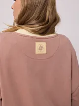 Sweater color ladrillo con cuello redondo en color crema. Estampado frontal con el texto 'Malibu Rusty' y un logo con forma de flor. Corte holgado.