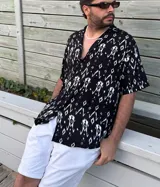 Camisa negra con estampado abstracto en blanco, de manga corta y cuello clásico.