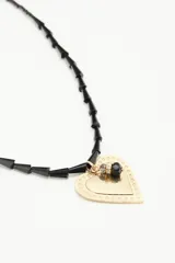 Collar de cadena de cuentas irregulares negras con dije central de corazón texturizado dorado y detalle de piedra negra.