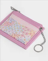 Tarjetero de cuerina color lila con estampado floral, cierre superior con cremallera y doble bolsillo frontal. Incluye mosquetón metálico para colgar.