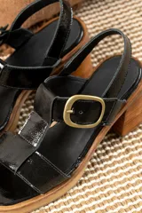 Sandalias de cuero charol negro con tiras entrecruzadas, hebilla dorada y tacón de madera.