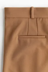 Pantalón ancho color marrón claro con pinzas, bolsillos laterales y trabillas para cinturón.