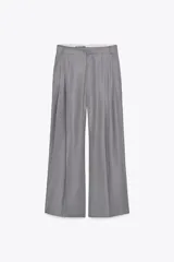 Pantalón gris de tiro alto con trabillas, doble pliegue, bolsillos laterales y tapetas en la espalda. Pernera ancha y cierre frontal con cremallera y gancho metálico.