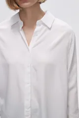 Camisa blanca de manga larga con cuello clásico y cierre frontal con botones. Corte recto y holgado.