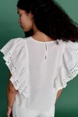 Blusa blanca de algodón con secciones en broderie. Modelo con mangas cortas de volados y cuello redondo con abertura de cerradura y botón oculto en la nuca.