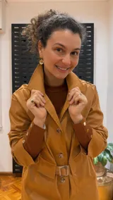 Gabardina color mostaza con cuello camisero, cierre frontal con botones y cinturón con hebilla.