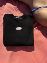Buzo negro oversize con cuello redondo y logo ovalado bordado en el pecho.