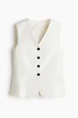Chaleco blanco con escote en V, cierre frontal con cuatro botones negros, bolsillos delanteros ribeteados y trabilla ajustable en la espalda.