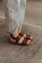 Sandalias de cuero marrón con tiras tejidas a mano y costuras a la vista, con base plana.