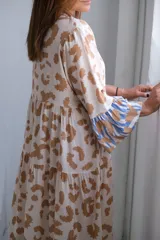Vestido midi de corte amplio, color beige con estampado abstracto en tonos marrones. Mangas tres cuartos con detalle de volados en puños con estampado a rayas celestes y marrones.