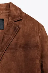 Blazer marrón de ante con cuello de solapa de muescas, manga larga, bolsillos de parche delanteros y cierre frontal con botones.