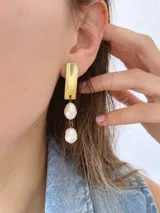 Aros colgantes con base rectangular dorada y dos perlas blancas unidas por aros de metal.