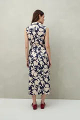 Vestido midi sin mangas con estampado floral y de hojas en tonos verde y marrón. Diseño cruzado tipo wrap con cuello sastrero y lazo ajustable en la cintura.