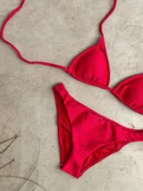 Conjunto de bikini verde esmeralda con textura acanalada. El corpiño es de triángulos movibles con tiras finas para atar al cuello y a la espalda, y tiene almohadillas desmontables. La bombacha es vedetina ancha con laterales fijos.