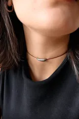 Gargantilla con tiento de hilo encerado color borgoña y dije de acero quirúrgico hipoalergénico plateado en forma de tubo.