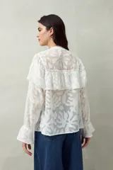 Camisa negra semitransparente de encaje bordado con diseño geométrico. Tiene silueta fluida, mangas largas y volados en el frente y los hombros.